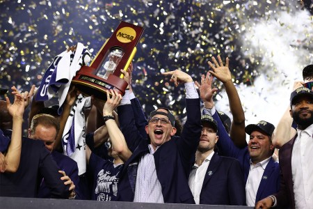 Dan Hurley and the UConn Huskies on a stage holding the national championship trophy.