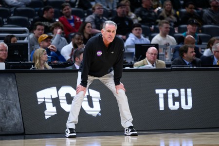 TCU coach Jamie Dixon standing on the sideline with his hands on his knees during a game.